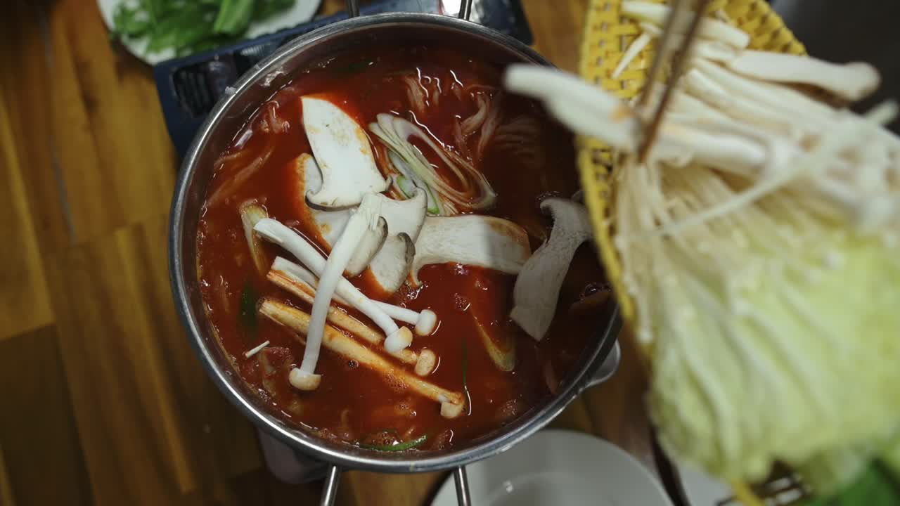 Bày trí nấm kim châm và nấm hương. Cảnh lẩu nấm trên bàn gỗ. Góc nhìn từ trên cao cho thấy nồi lẩu đầy nấm và nước dùng trên bàn mộc mạc.