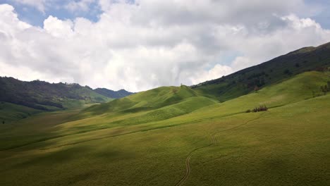 aerial 4k drone footage of the tranquil allure of a lush green valley nestled among mist-covered hills, enhanced by the soothing patter of cloudy sky