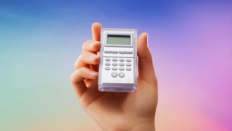 hand holding a small calculator against a pastel gradient background