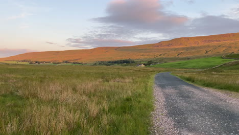 establishing handheld shot of side of whernside mountain and fields at golden hour sunrise