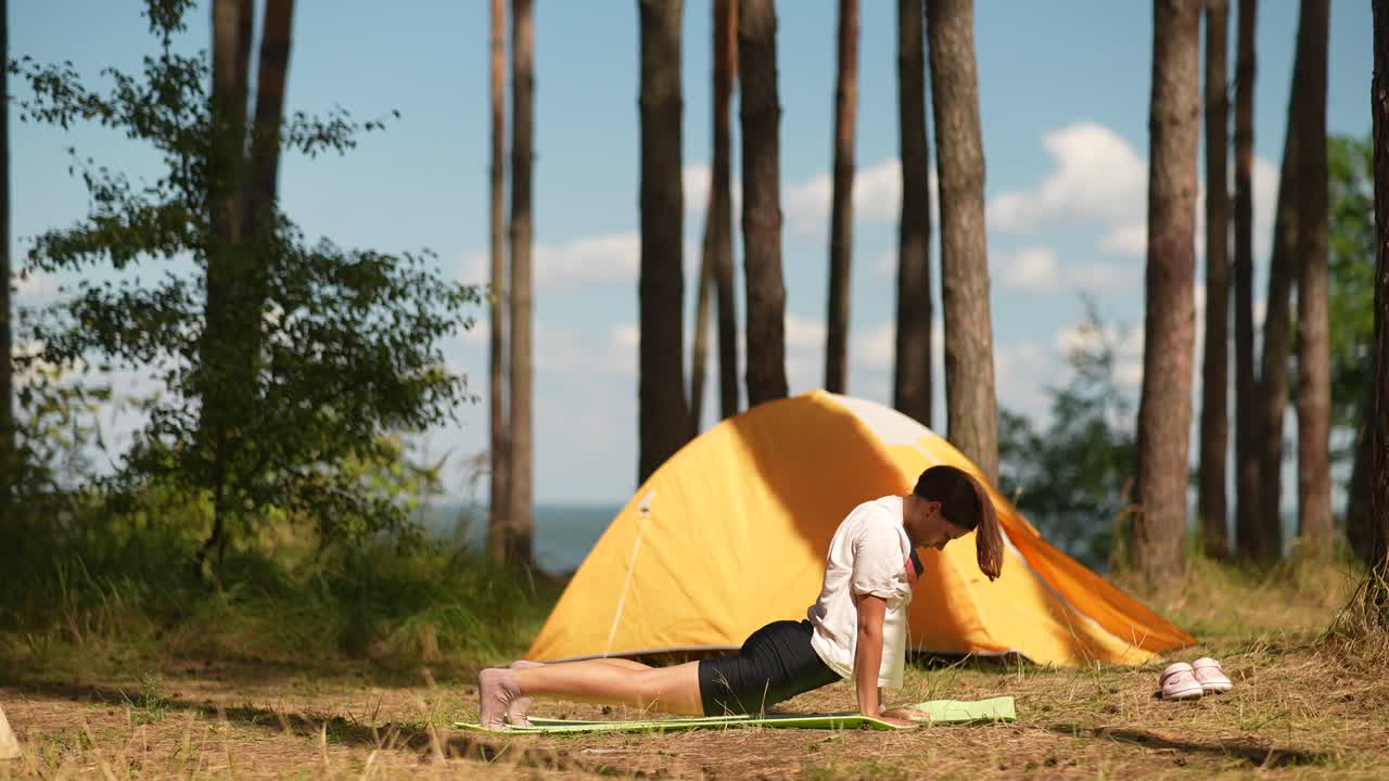 캠핑 텐트 근처 의 숲 에서 요가 를 연습 하는 여자