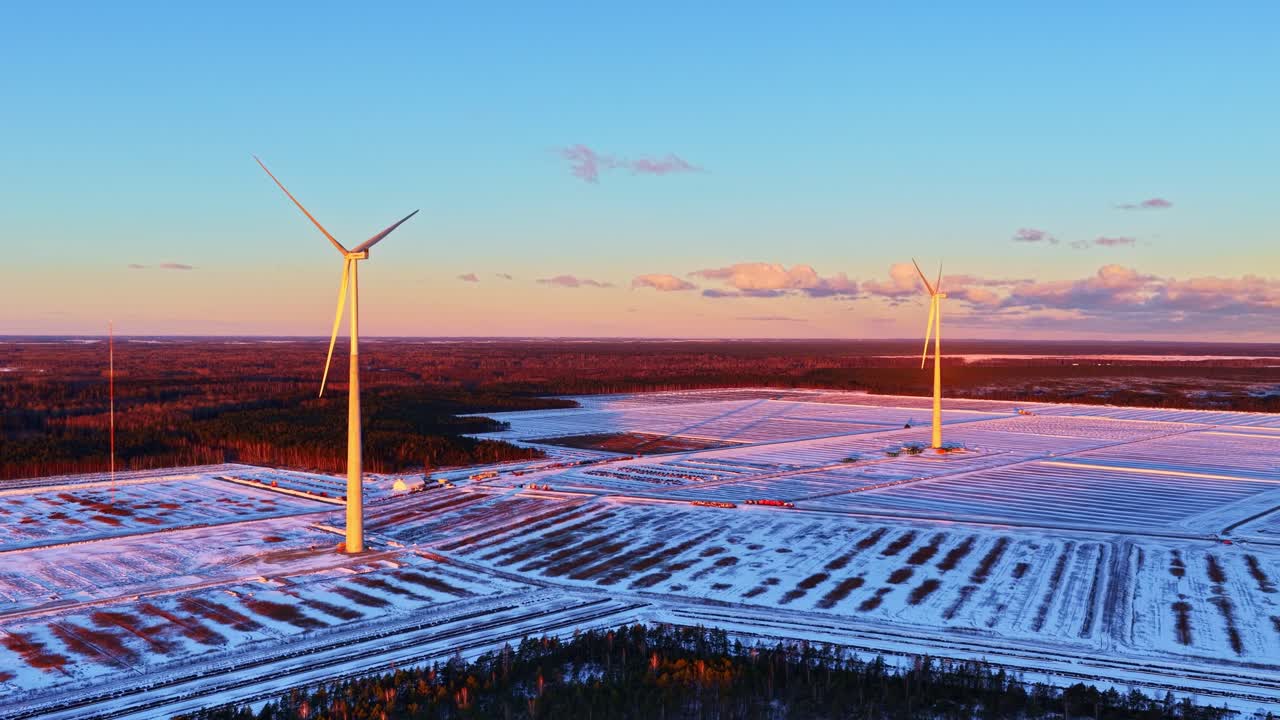 En række vindmøller strækker sig over et snedækket terræn under en glødende solnedgang om vinteren, luft Dolly