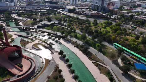 an artificial river in the middle of a dense city in nuevo leon, mexico. in the background, you can see the subway and cars traveling through the streets on a sunny day, . 4k 60fps