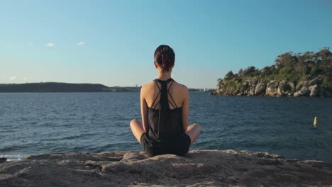 plano amplio de una mujer joven sentada con las piernas cruzadas por el agua meditando