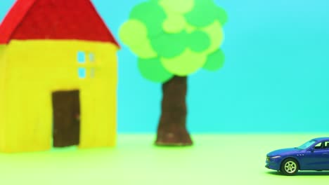 blue modern car passing by yellow house and tree - stop motion