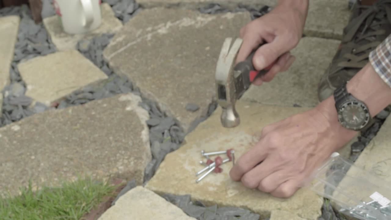 Workman hands hammering nails into nail hook cable clip on concrete floor