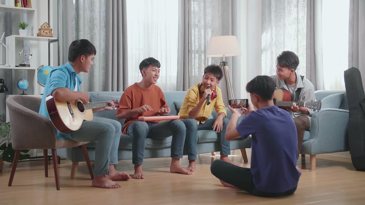 젊은 아시아 친구 그룹이 스마트폰을 사용하면서 노래하고 악기를 연주하고 집에서 라이브 스트리밍을 하고 있습니다.