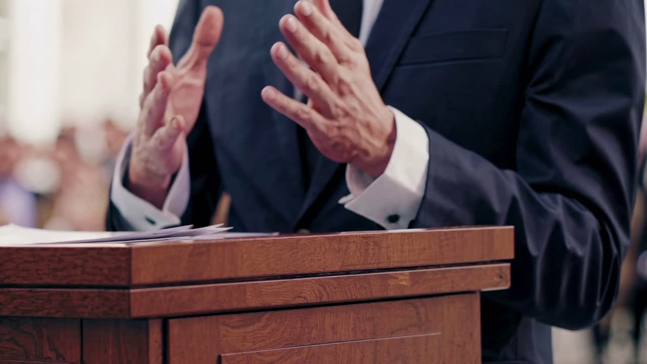 Close-up video angle of a speaker's hands gesturing passionately at a podium, conveying authority