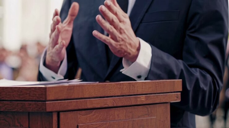 Close-up video angle of a speaker's hands gesturing passionately at a podium, conveying authority