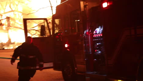 a firetruck pulls up and parks next to a huge fire as a fireman jumps out to fight the inferno