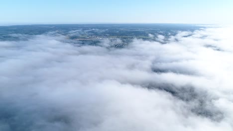 Vuelo-Sobre-Nubes-Brumosas-A-La-Luz-Del-Sol-De-La-Mañana-Con-Poca-Gloria-Y-Paisaje-Urbano-Bajo-Las-Nubes