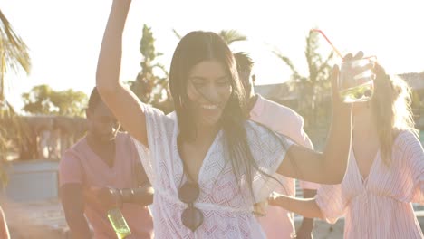 happy diverse group of friends dancing holding cocktails at beach