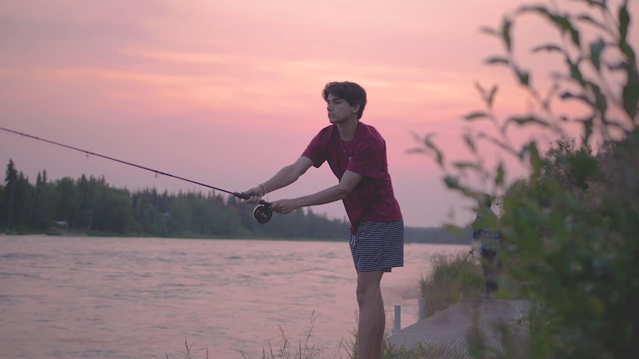 A teenager fishing during sunset on the Kenai River, in Alaska.