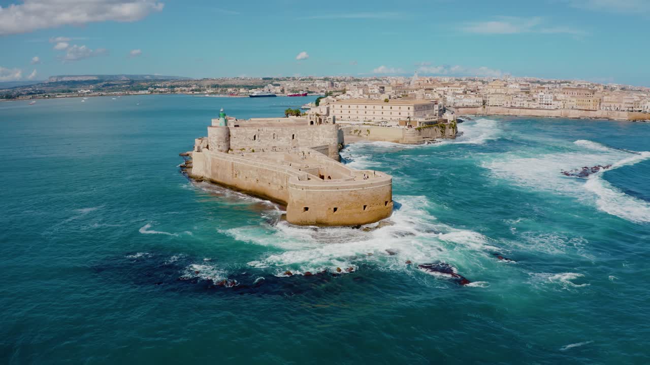 Drone shot of medieval castle in Ortigia island. Historic old town in Syracuse. Castello Maniace fortress in the middle of Mediterranean sea with large waves crashing into the walls. UNESCO heritage.