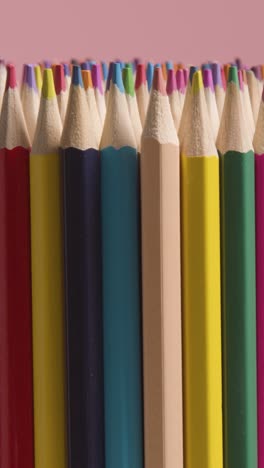 vertical video studio shot of rotating multi-coloured pencils against pink background