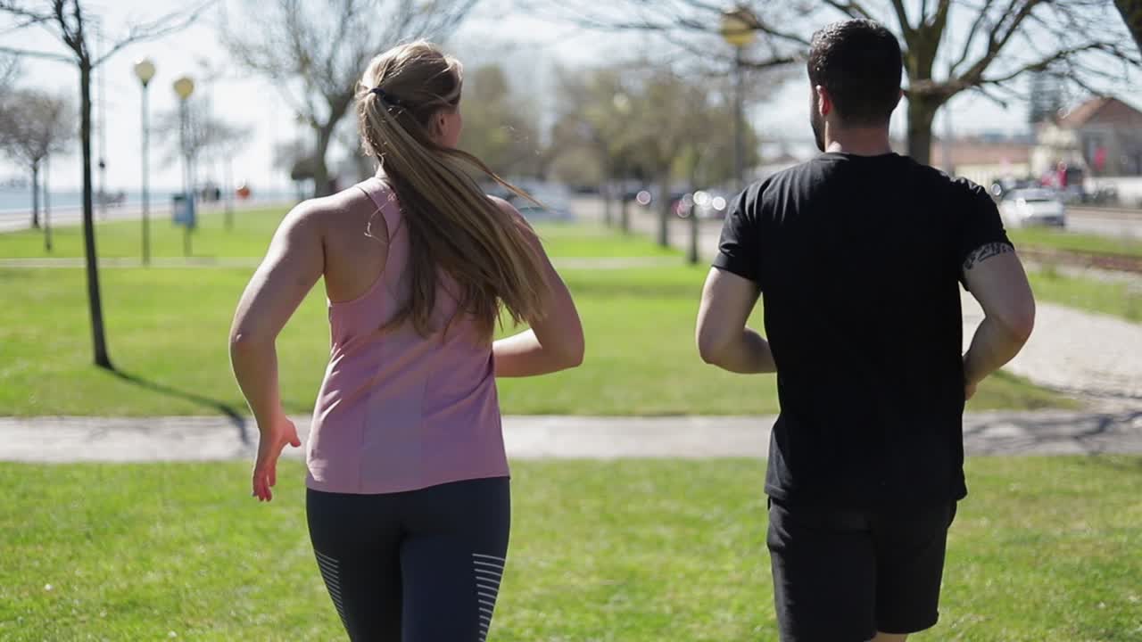 vista trasera de una joven pareja corriendo en el parque.