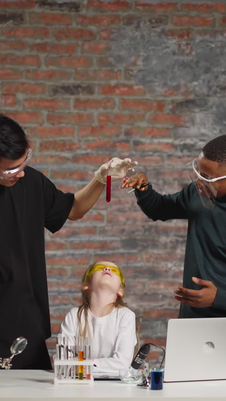 Asian and African-American teachers show test tube with blood to girl student recording video for blog at online fun chemistry lesson in studio
