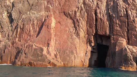 Hole-in-rock-formation-of-jagged-coast-of-Calanques-de-Piana-seen-from-moving-boat-on-Mediterranean-Sea-in-Corsica-island-in-summer-season,-France