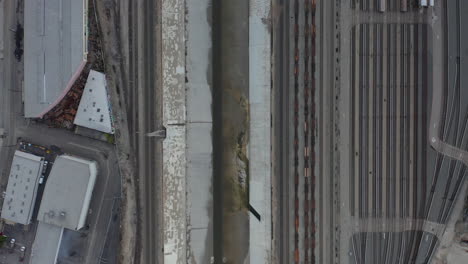 AERIAL:-Overhead-,-Birds-Eye-View-on-Los-Angeles-River-with-Water-on-Cloudy-Overcast-Sky-next-to-Train-Tracks