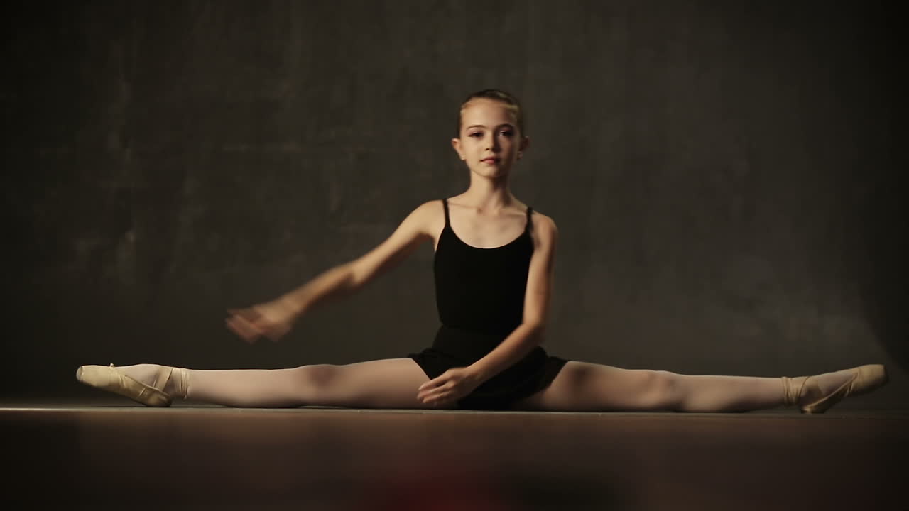 Little adorable young ballerina in tutu and pointe in the black studio