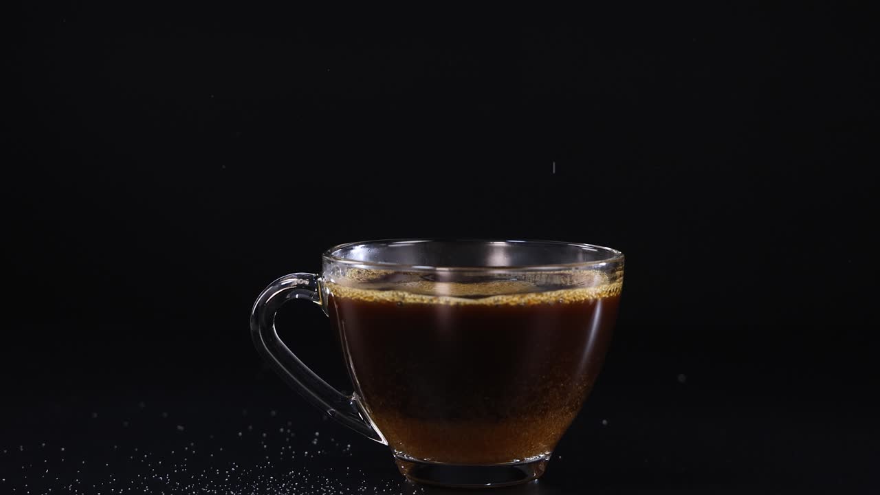 Sugar cascades into a glass cup of tea against a dark backdrop, highlighting the contrast and motion