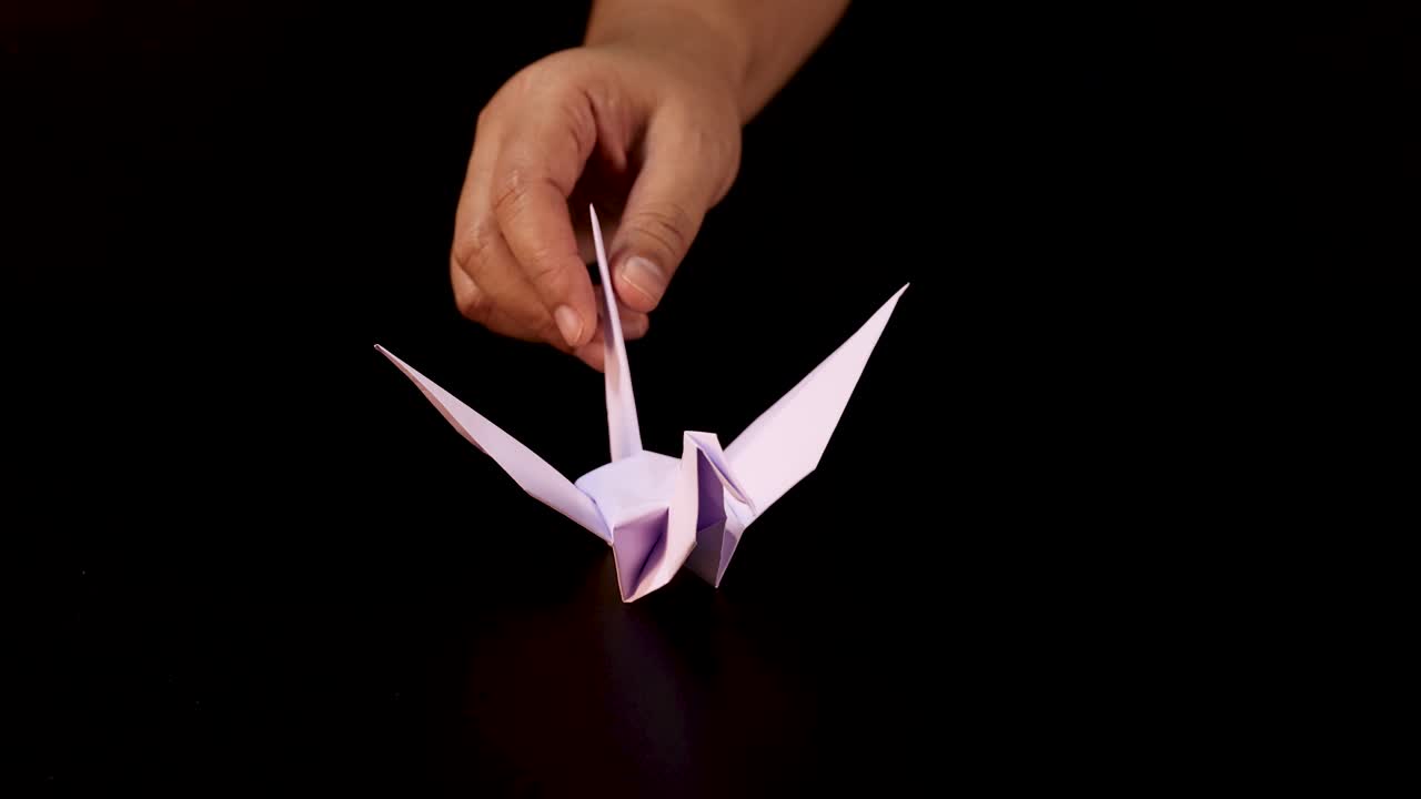 Human hand sets completed origami crane on dark surface, dramatic lighting, close-up view