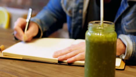 Man-writing-in-his-dairy-with-juice-on-table
