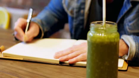 man writing in his dairy with juice on table