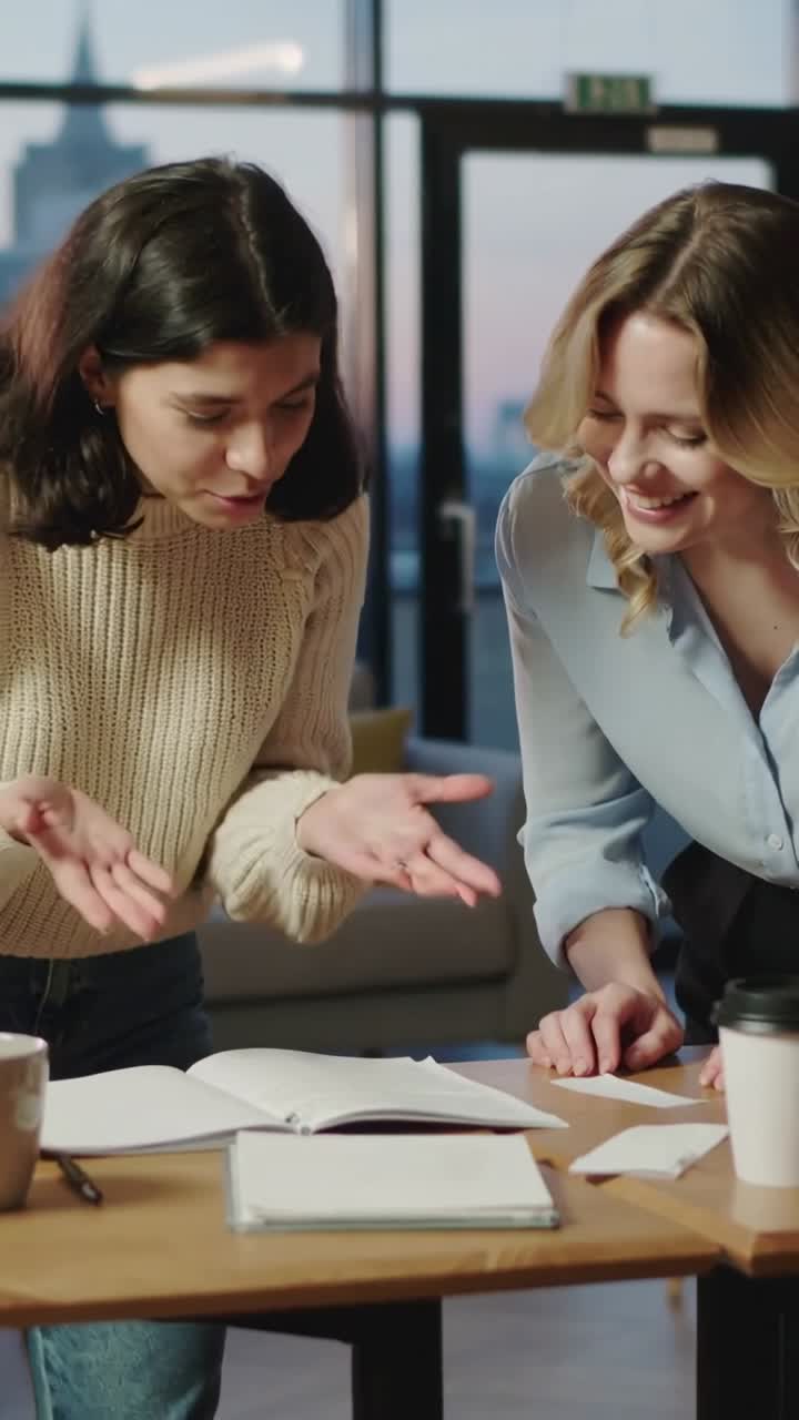 Due donne, una con maglione beige e l'altra con camicetta blu, si sporgono indicando e confermando documenti in un salotto con un quaderno.