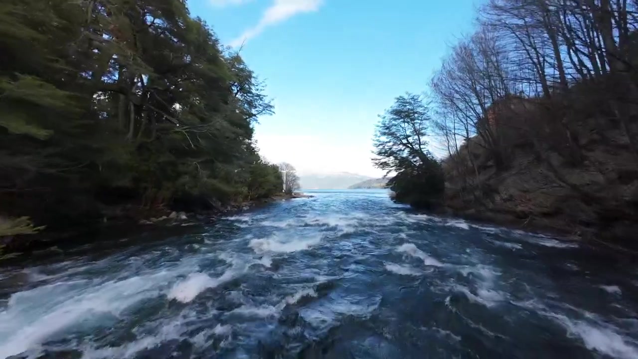 Fiume turchese che scorre tra sponde boscose con riva rocciosa a Villa La Angostura, Patagonia, panoramica aerea con drone.