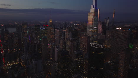 Ascending-forwards-fly-above-city-at-dusk.-Modern-glossy-skyscrapers-reflecting-colourful-twilight-sky.-Manhattan,-New-York-City,-USA