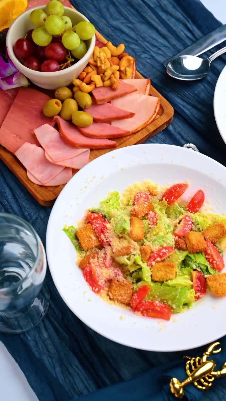 Due piatti di insalata Caesar su tovaglia blu con posate. Inquadratura dall'alto di due insalate fresche con crostini di pane e pomodorini.