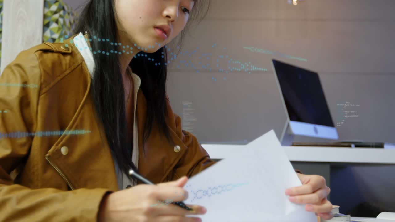 Student writing with pen referring notes, flipping pages, glancing at PC studying amid blue overlay