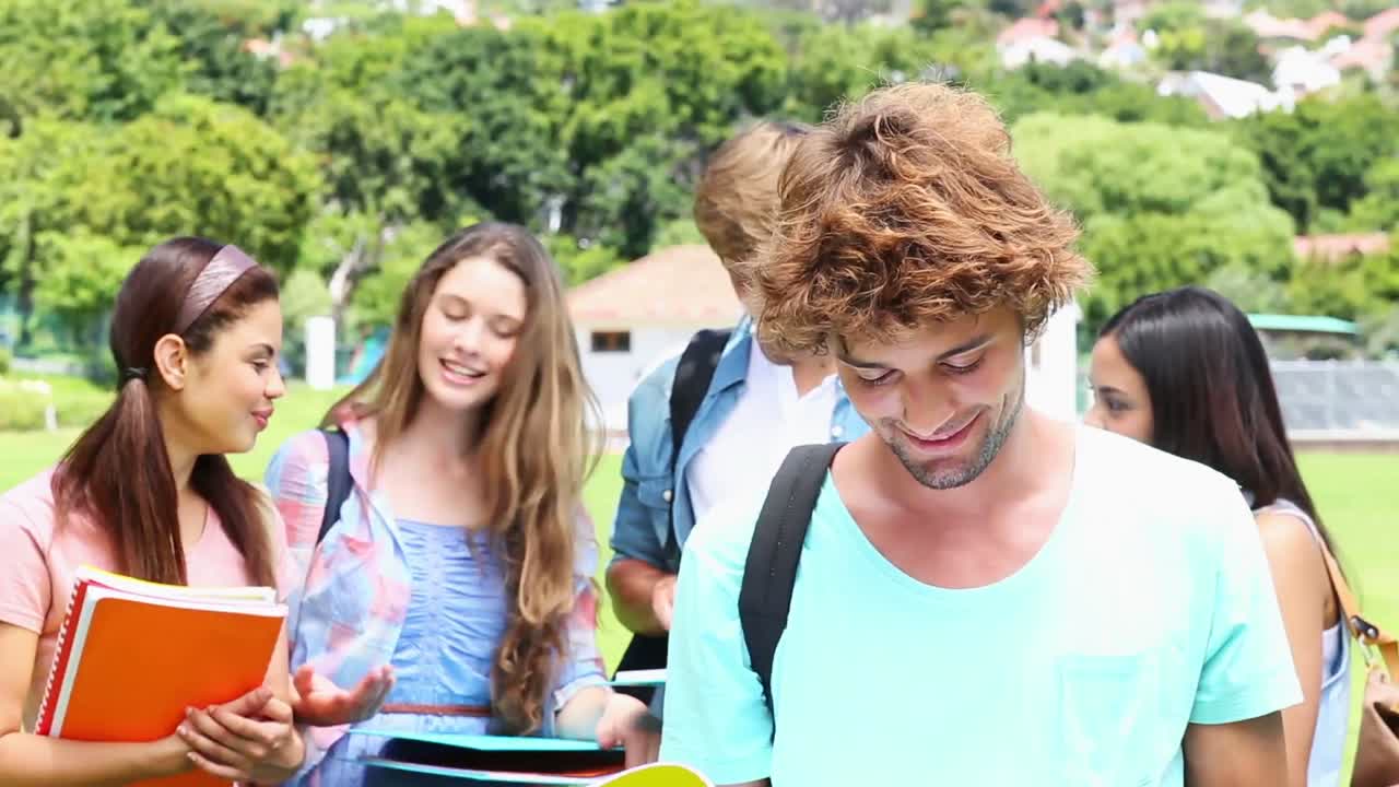 estudiante guapo sonriendo a la cámara con sus compañeros de clase detrás