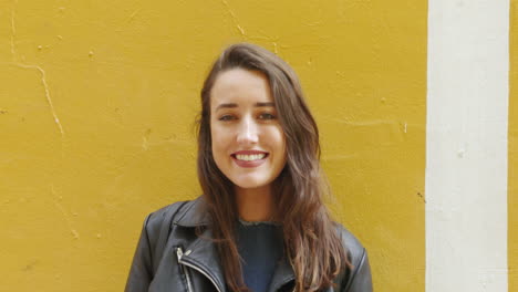 slow motion portrait of a fashionable, young woman smiling brightly in front of a yellow wall