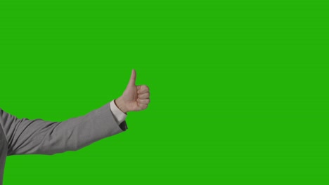 close up of arm of businessman in suit giving thumbs up gesture against green screen