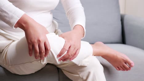 close up of woman sitting on the sofa doing self-massage on the knee for relieving pain