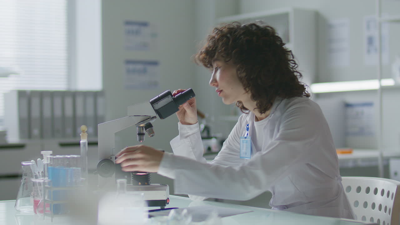 Female Chemist Taking Notes during Microscopic Research in Scientific Laboratory