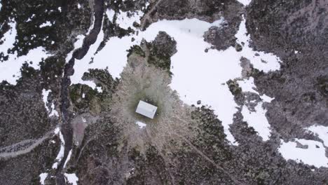 aerial drone footage slowly descending towards a remote bothy with beautiful patterns in the grass, snow patches, a river and frosty moorland in winter