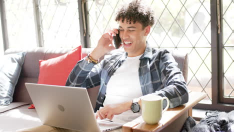 biracial man working from home using laptop and talking on smartphone, slow motion