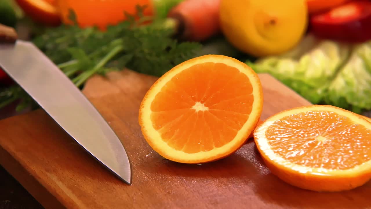 Fetta d'arancia caduta su tagliere con coltello da cucina e altri pezzi tagliati preparati per insalata fresca