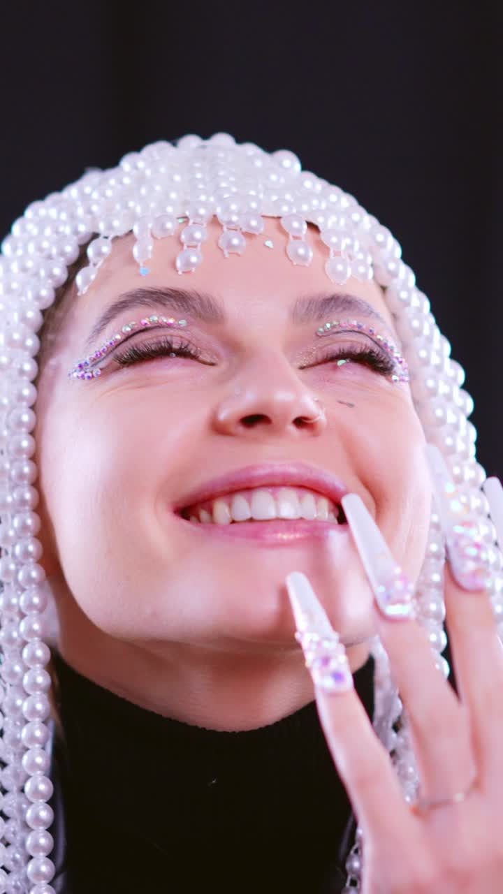 Close-up portrait of a woman with a pearl headpiece, glitter makeup, and long decorated nails