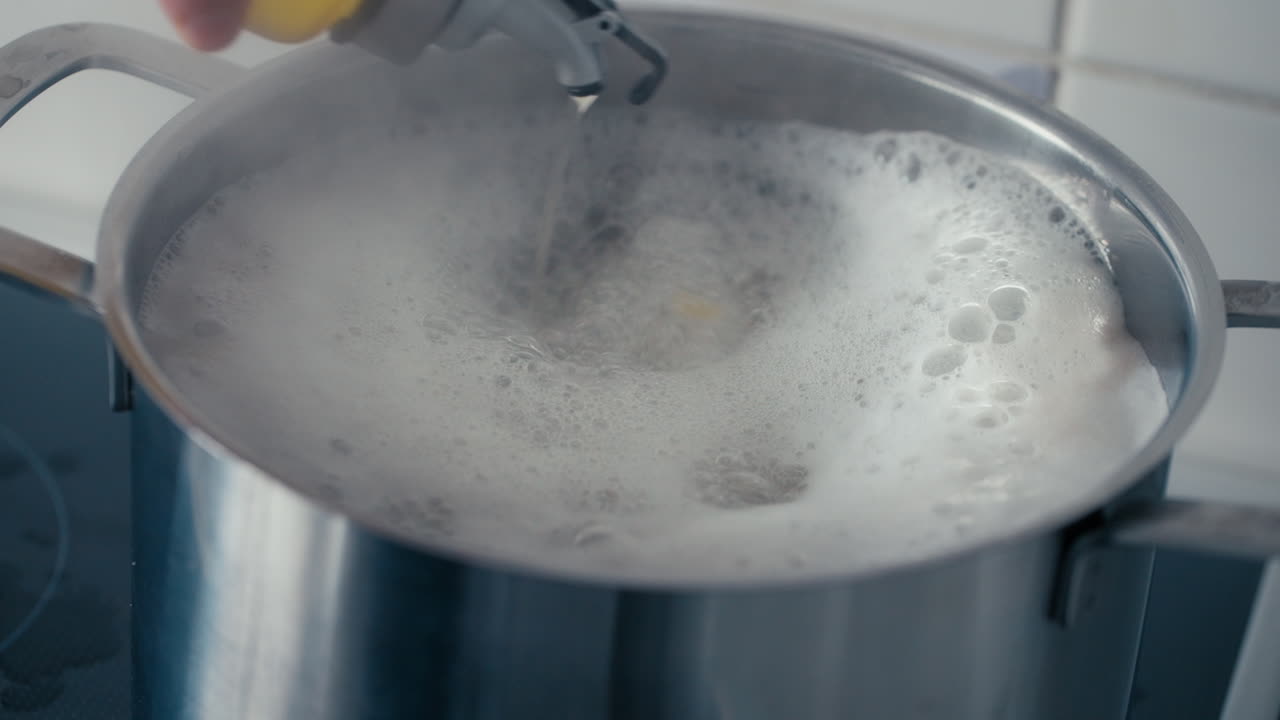 Primo piano - Aggiunta di olio d'oliva alla grande pentola di acqua bollente per le tagliatelle al rallentatore di giorno.