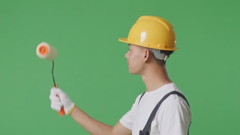 Close Up Of Side View Asian Man Painter Wearing Safety Helmet Painting And Smiling In The Green Screen Background Studio