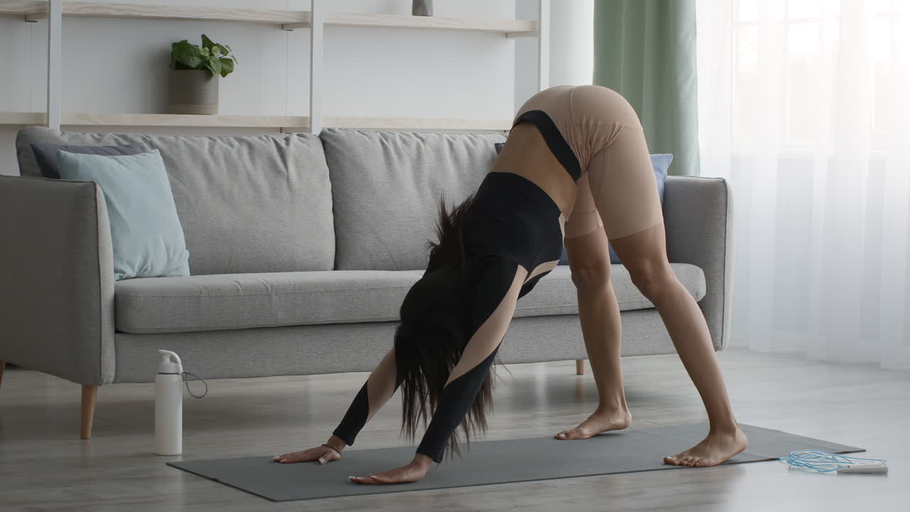 mujer haciendo la postura de yoga del perro hacia abajo en casa