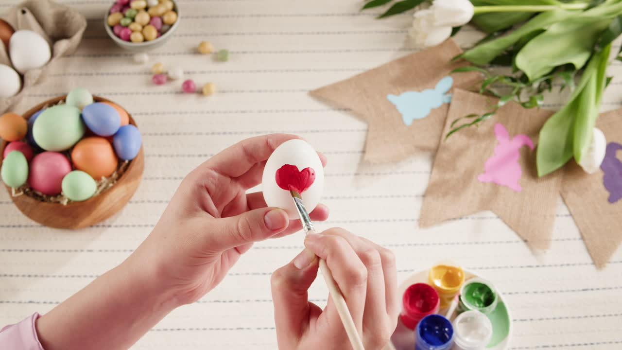 Mani che dipingono un motivo a cuore rosso su un uovo di Pasqua