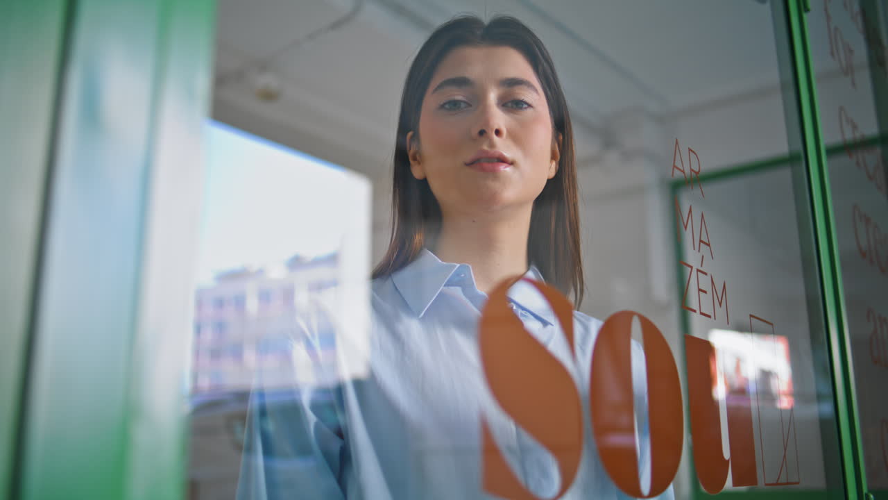 hermosa mujer de ventas mira a través de la ventana de vidrio de primer plano. propietario de una pequeña empresa