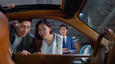 couple with attractive auto dealer in a suit presenting new car model to his client