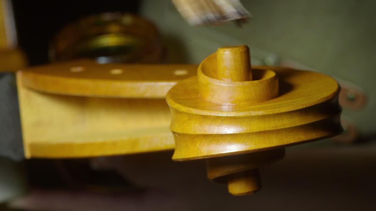 Luthier carefully applying varnish on a cello scroll using a brush, showcasing the craftsmanship and precision involved in musical instrument making