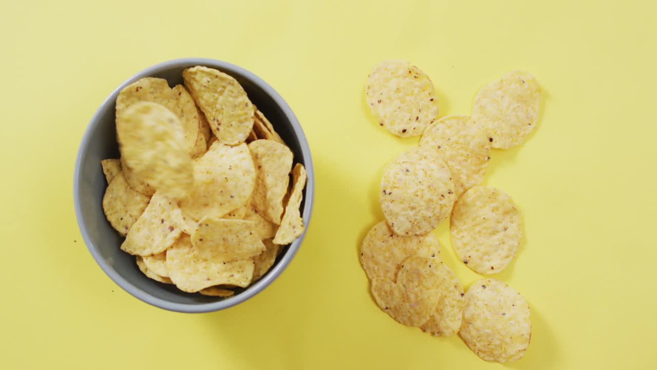 Close up of potato chips in a bowl on yellow surface